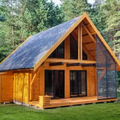Nowoczesny domek całoroczny 20m2 z drewnianą elewacją i dużymi oknami, otoczony zielenią lasu.