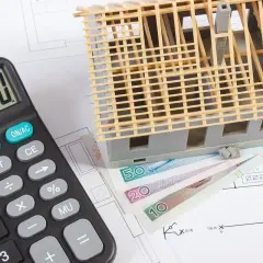 Kalkulator, makieta domu wielorodzinnego i polskie banknoty na planach budowlanych. Zastanawiasz się, ile kosztuje budowa domu wielorodzinnego?