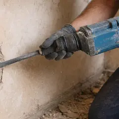 Ręce w rękawicach używają młota udarowego, by usunąć baranka ze ściany.