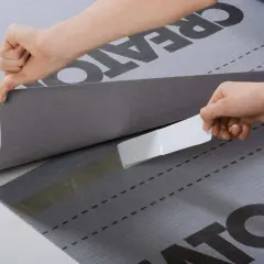 Dwie ręce przyklejają taśmę do membrany dachowej. Wybór odpowiedniej membrany to klucz do trwałego dachu.