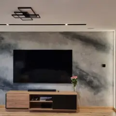 Nowoczesny salon z telewizorem na tle ściany z efektem betonu, jak zrobić tynk dekoracyjny.
