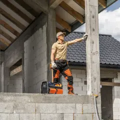Budowlaniec sprawdza fundament pod domek 35m2. W tle widać dach i ściany z bloczków.