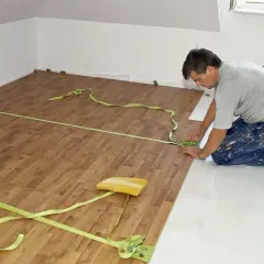 Układanie paneli podłogowych w mieszkaniu 50m2. Remont trwa, a wykonawca precyzyjnie dopasowuje deski.