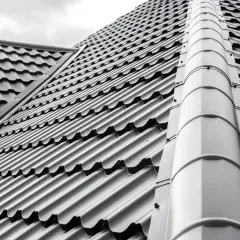 Szary dach z blachodachówki, która jest tańsza niż dachówka ceramiczna. Widoczny grzbiet dachu i jego nachylenie.