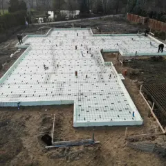 Przygotowywane fundamenty pod domek letniskowy. Płyta izolacyjna z siatką zbrojeniową i rurami.