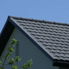 Szary dach z dachówki ceramicznej, idealny do obliczenia, ile dachówek na m2 roben. W tle błękitne niebo i fragment ściany domu.