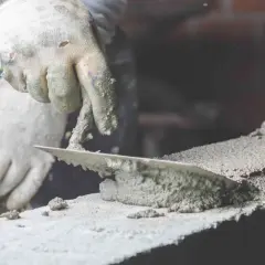 Ręka w rękawicy nakłada zaprawę murarską kielnią na cegłę. To kluczowy etap, jak zrobić zaprawę murarską.