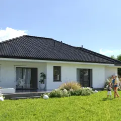 Marzysz o domu? Sprawdź, ile kosztuje budowa domu 150m2. Rodzina cieszy się ogrodem przy nowoczesnym domu.