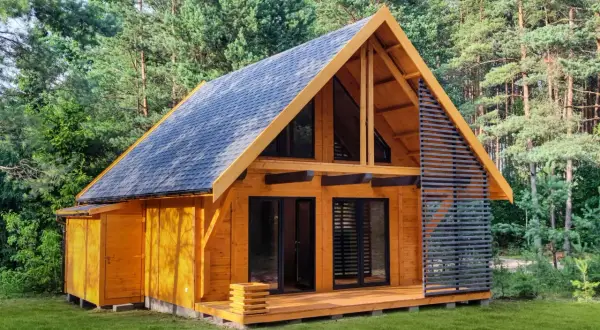 Nowoczesny domek całoroczny 20m2 z drewnianą elewacją i dużymi oknami, otoczony zielenią lasu.