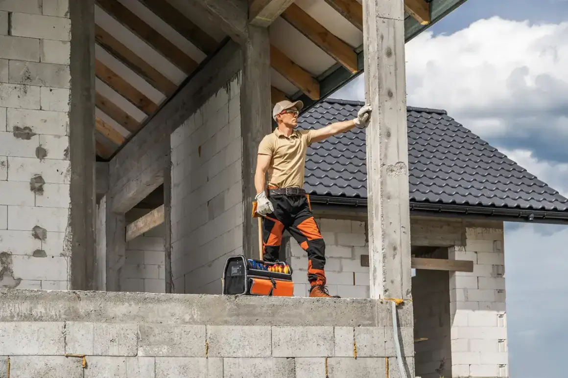 Budowlaniec sprawdza fundament pod domek 35m2. W tle widać dach i ściany z bloczków.