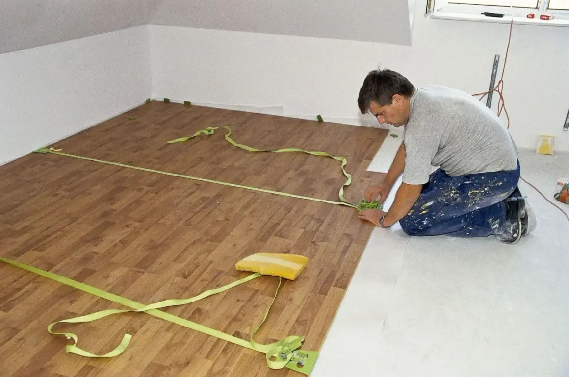 Układanie paneli podłogowych w mieszkaniu 50m2. Remont trwa, a wykonawca precyzyjnie dopasowuje deski.