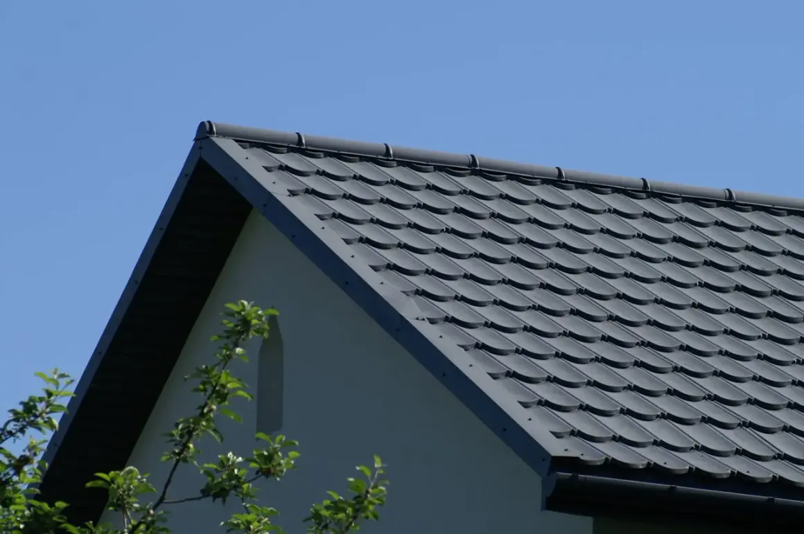 Szary dach z dachówki ceramicznej, idealny do obliczenia, ile dachówek na m2 roben. W tle błękitne niebo i fragment ściany domu.