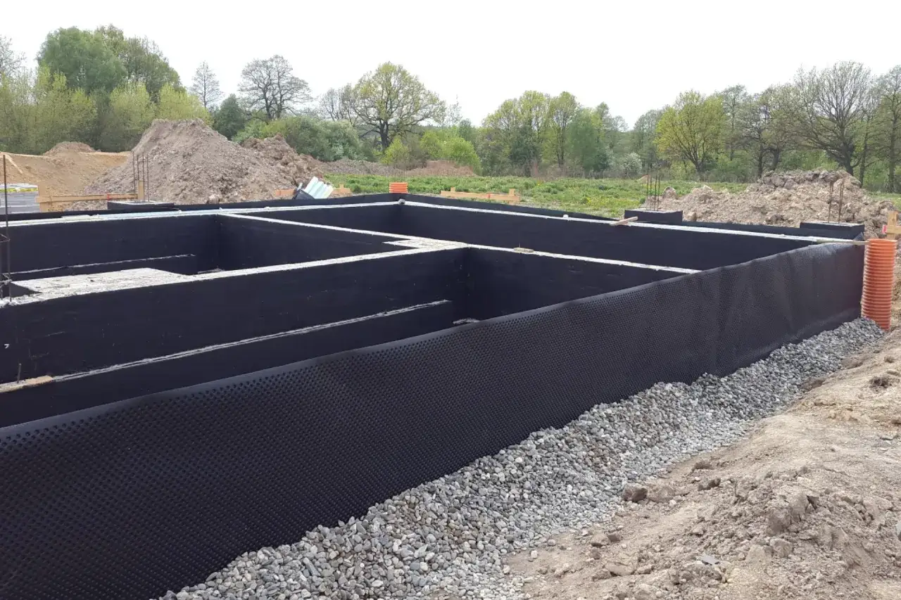 Fundament pod domek narzędziowy w trakcie budowy. Widoczne izolowane ściany fundamentowe i podsypka żwirowa.