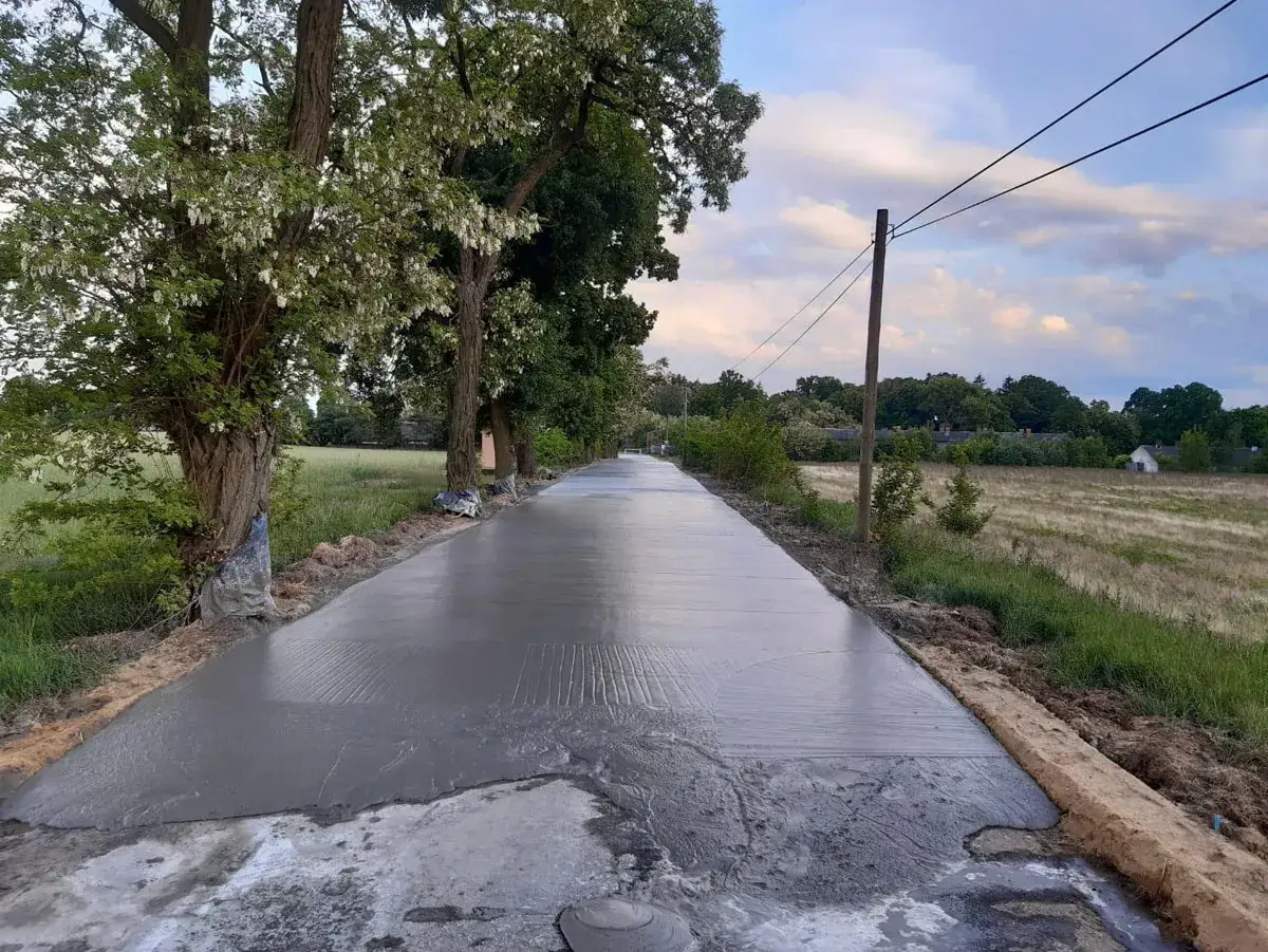 Świeżo wylany beton na drodze, otoczony drzewami. Zastanawiasz się, ile kosztuje kilometr asfaltu?