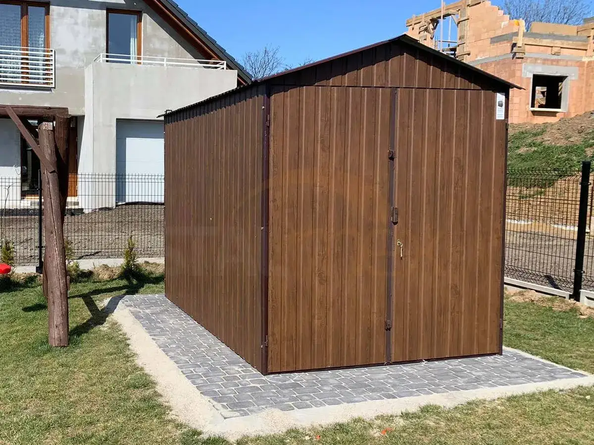 Brązowy domek narzędziowy na podjeździe z kostki brukowej. Idealne miejsce co pod domek narzedziowy, by schować narzędzia ogrodowe.