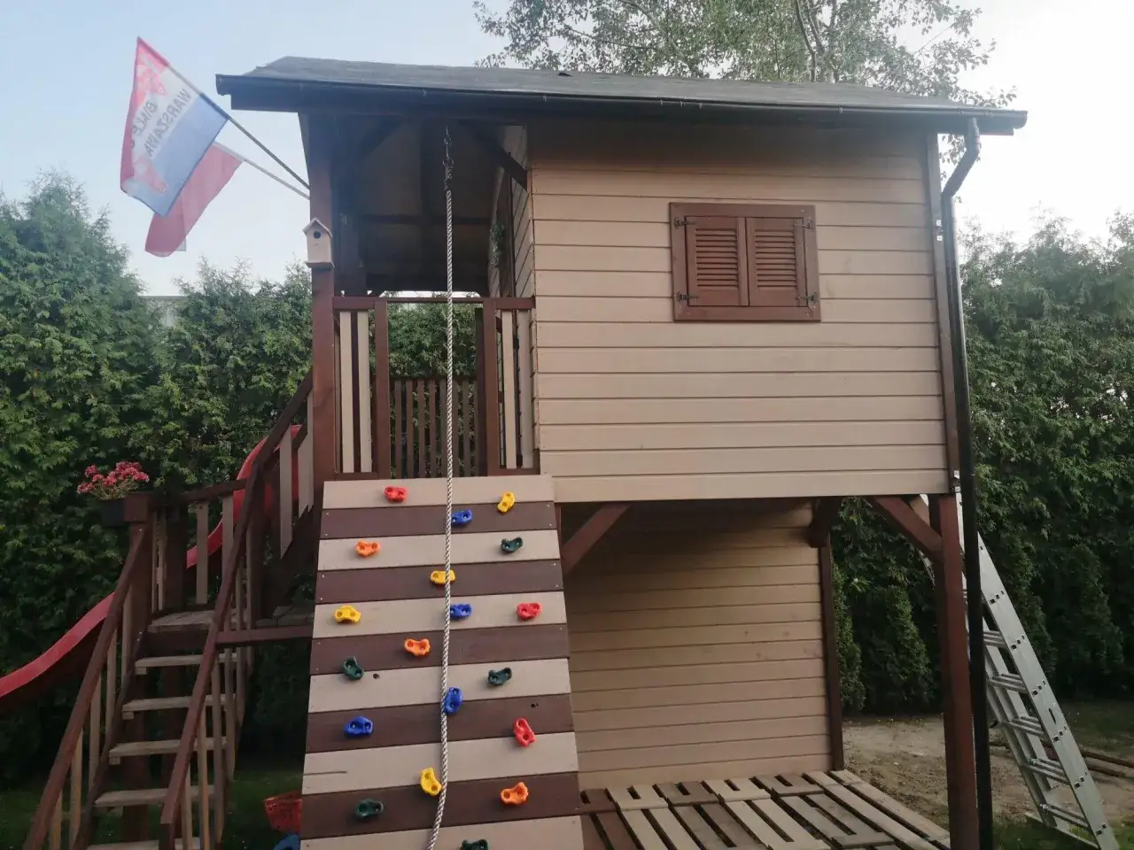 Kolorowe chwyty wspinaczkowe na schodach do domku dla dzieci. Obok zjeżdżalnia i drabinka.