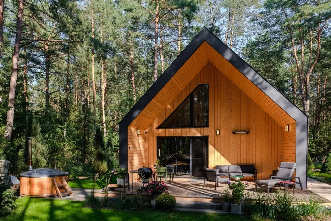 Nowoczesny drewniany dom w lesie z bali, z tarasem i jacuzzi. Zastanawiasz się, ile kosztuje budowa domu drewnianego pod klucz?