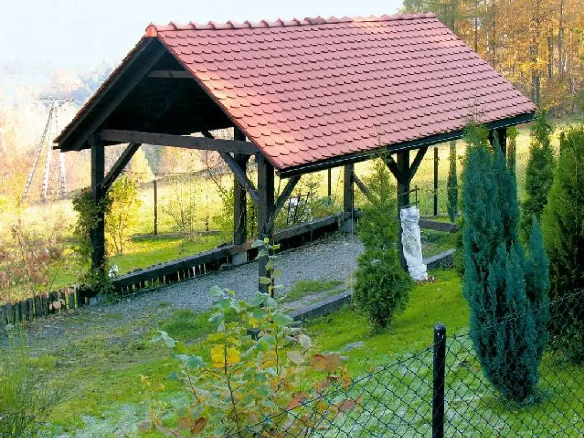 Solidne wiaty garażowe drewniane z czerwonym dachem, otoczone zielenią i jesiennym krajobrazem.