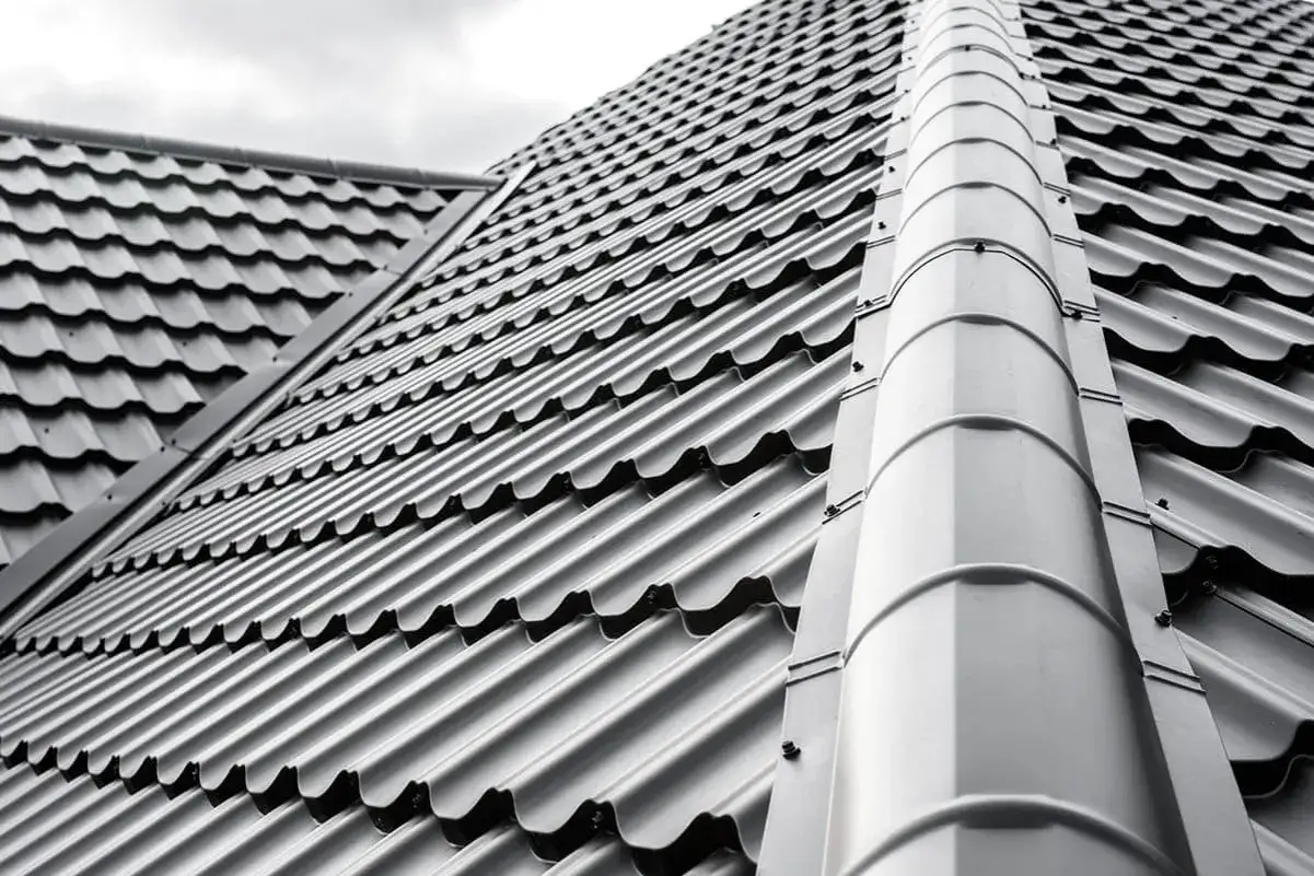 Szary dach z blachodachówki, która jest tańsza niż dachówka ceramiczna. Widoczny grzbiet dachu i jego nachylenie.